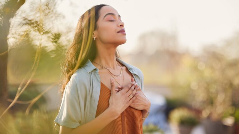 Young latin woman with hand on chest breathing in fresh air in a beautiful garden